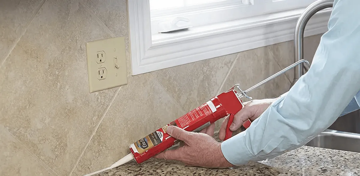 Handyman applying caulk along a kitchen backsplash and countertop seam in Aurora, IL